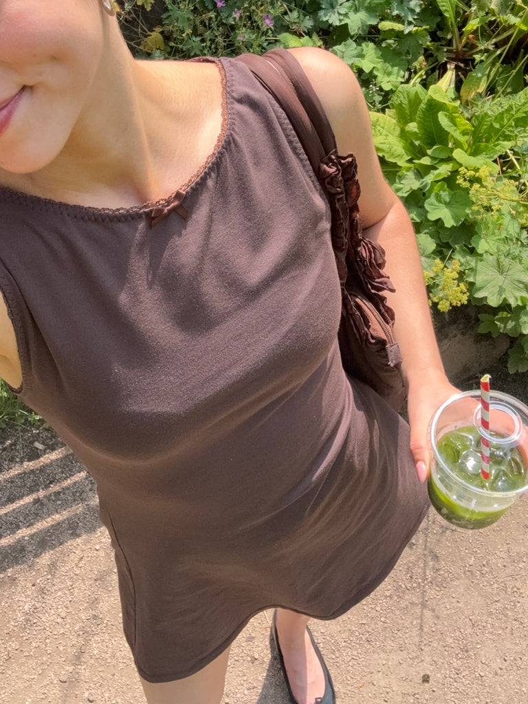 Woman in a brown sleeveless top holding a matcha outdoors.